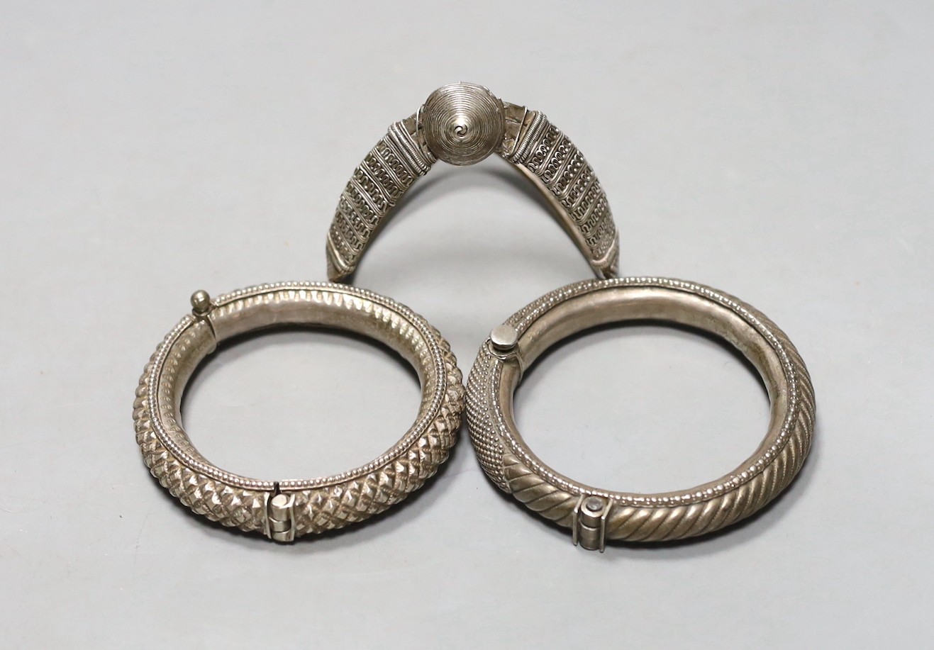 Two 20th century Indian white metal hinged bracelets and a similar shaped bangle.